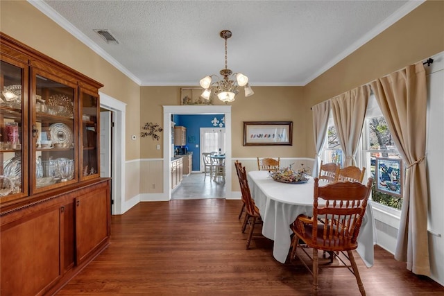 dining space featuring visible vents, crown molding, a chandelier, a textured ceiling, and dark wood-style flooring