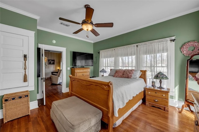 bedroom with visible vents, baseboards, wood finished floors, and crown molding