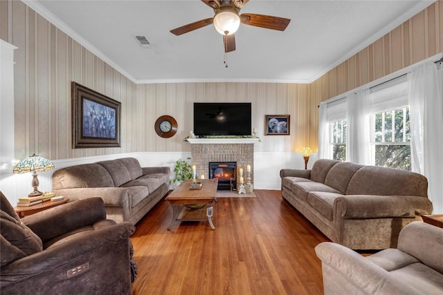 living room with a ceiling fan, wood finished floors, visible vents, a fireplace, and ornamental molding