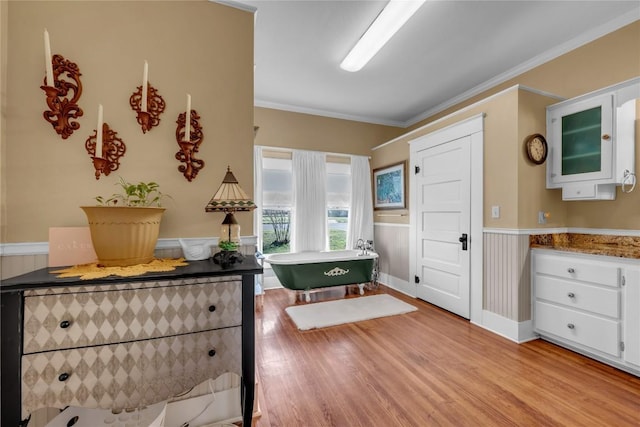 bathroom featuring a wainscoted wall, a freestanding bath, wood finished floors, and ornamental molding