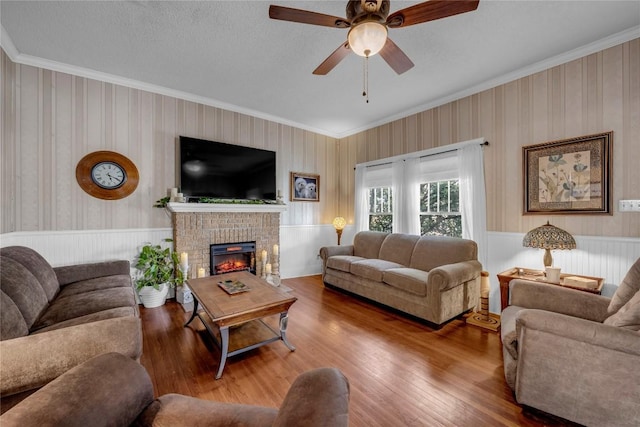 living area featuring a brick fireplace, crown molding, ceiling fan, and wood finished floors