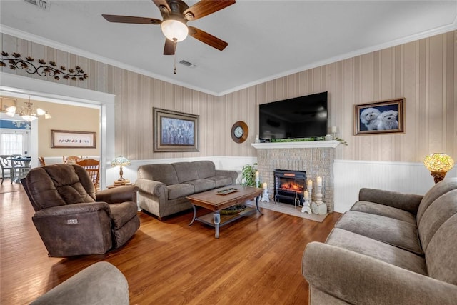 living area featuring visible vents, a brick fireplace, crown molding, ceiling fan with notable chandelier, and wood finished floors