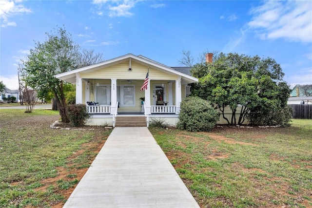 bungalow with a chimney, covered porch, and a front lawn