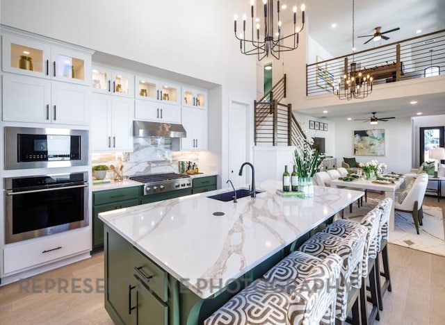 kitchen with ceiling fan with notable chandelier, under cabinet range hood, a sink, open floor plan, and stainless steel appliances