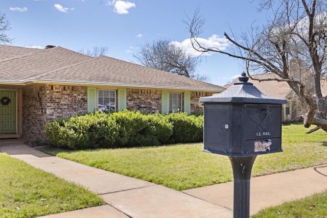 view of front of property featuring brick siding, a front lawn, and roof with shingles