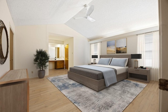 bedroom with lofted ceiling, light wood-style flooring, ensuite bath, ceiling fan, and a textured ceiling