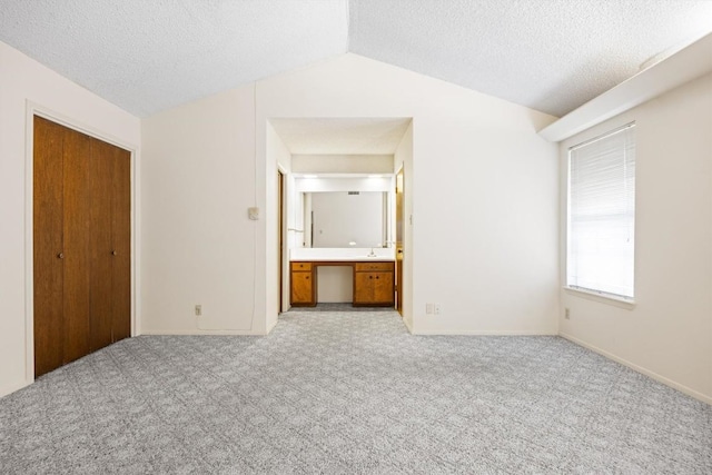 unfurnished bedroom featuring a textured ceiling, light colored carpet, and vaulted ceiling