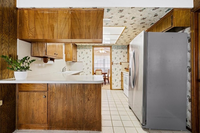 kitchen featuring brown cabinetry, wallpapered walls, a peninsula, stainless steel fridge with ice dispenser, and light countertops