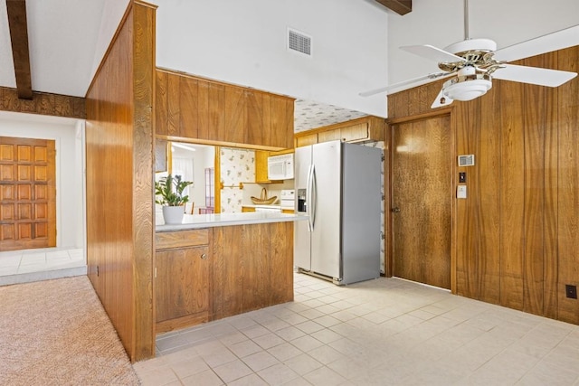 kitchen with white microwave, wooden walls, fridge with ice dispenser, brown cabinetry, and a ceiling fan