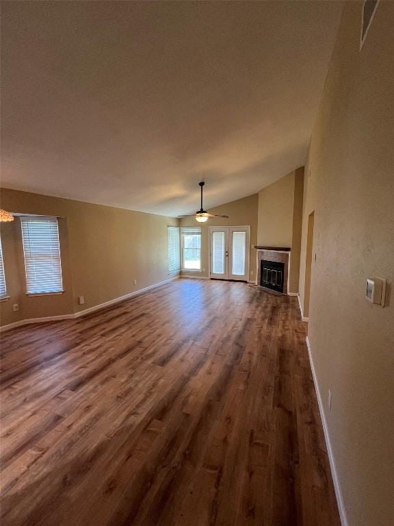 unfurnished living room with ceiling fan with notable chandelier, a healthy amount of sunlight, dark wood finished floors, and vaulted ceiling