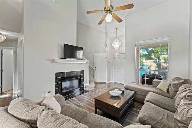 living area featuring ceiling fan, baseboards, a fireplace, a towering ceiling, and wood finished floors