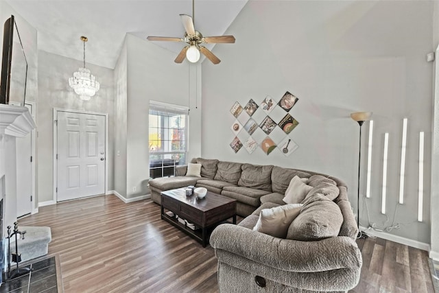 living area featuring ceiling fan with notable chandelier, a high ceiling, baseboards, and wood finished floors