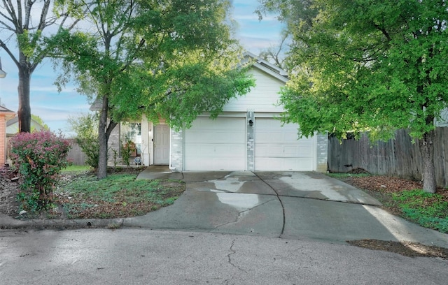 view of property hidden behind natural elements featuring concrete driveway, an attached garage, and fence