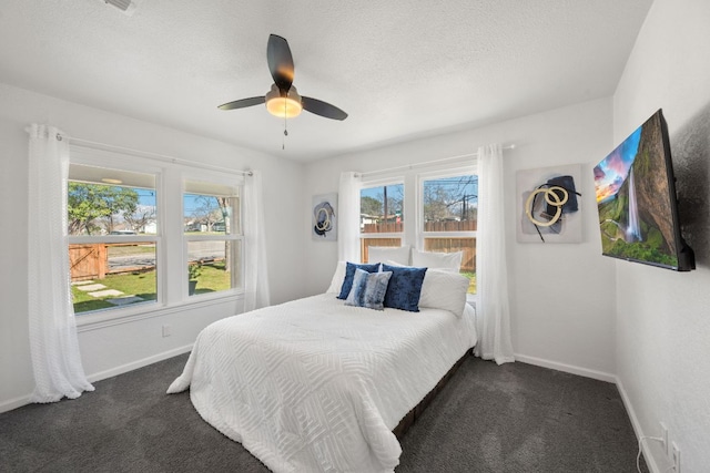 bedroom with a textured ceiling, a ceiling fan, baseboards, and dark colored carpet