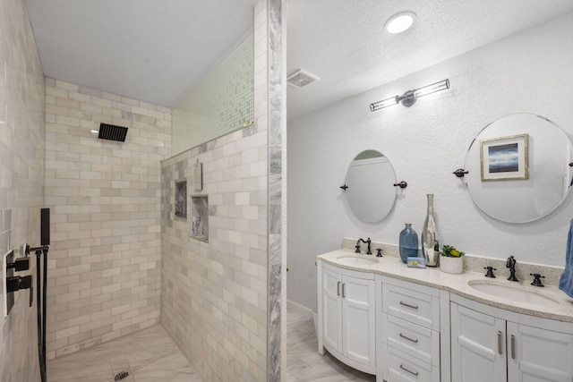 full bathroom featuring a tile shower, double vanity, a textured ceiling, and a sink