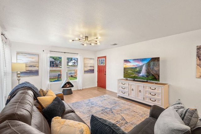 living area with visible vents, baseboards, a chandelier, light wood-style floors, and a textured ceiling