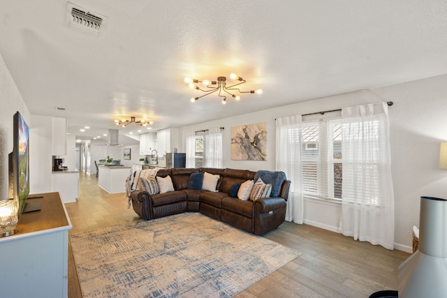 living room featuring a notable chandelier, baseboards, light wood-type flooring, and visible vents