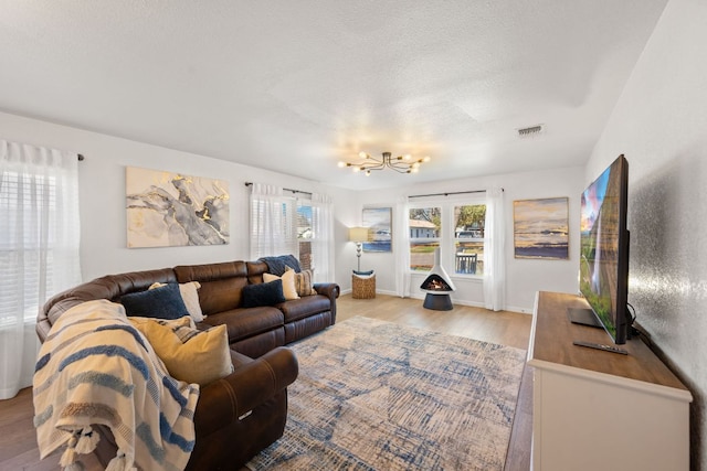 living area with visible vents, a textured ceiling, light wood finished floors, baseboards, and a chandelier