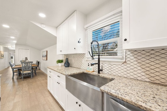 kitchen featuring light wood finished floors, lofted ceiling, a sink, decorative backsplash, and white cabinetry