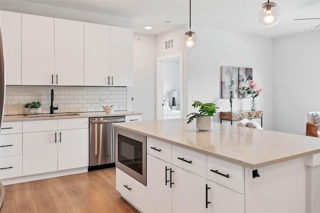 kitchen with light wood-style flooring, decorative backsplash, a sink, built in microwave, and dishwasher