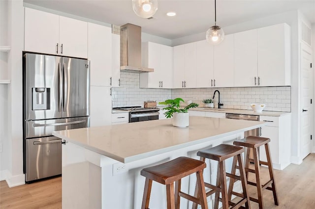 kitchen with light wood-style flooring, a kitchen breakfast bar, appliances with stainless steel finishes, and wall chimney exhaust hood