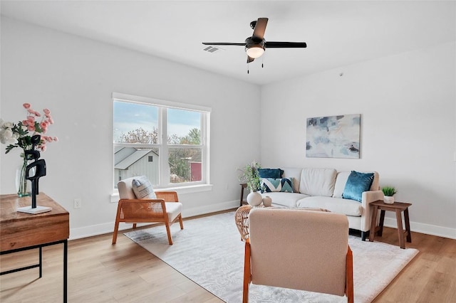 living room with a ceiling fan, visible vents, light wood-type flooring, and baseboards