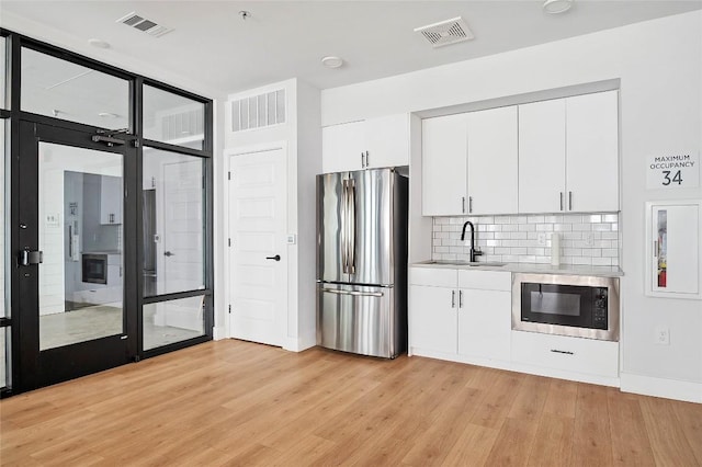 kitchen with light wood finished floors, visible vents, black microwave, freestanding refrigerator, and a sink