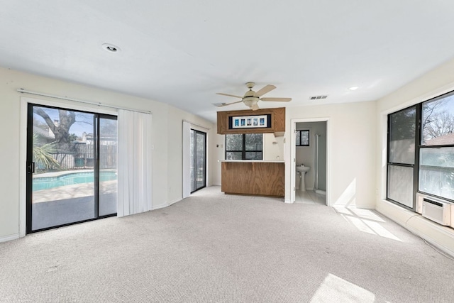 unfurnished living room featuring a healthy amount of sunlight, visible vents, carpet floors, and ceiling fan