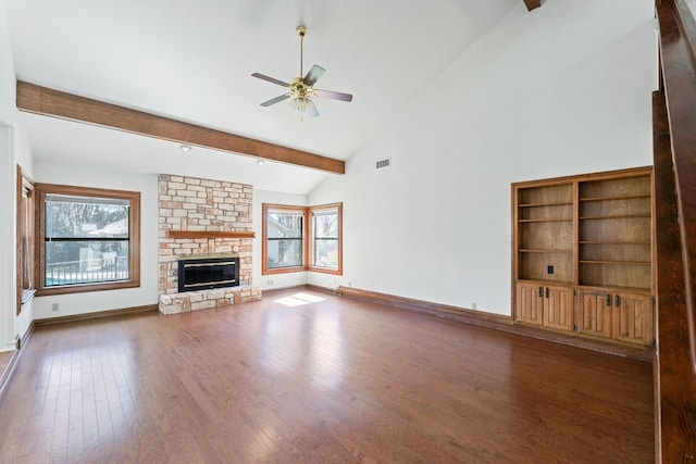 unfurnished living room with a wealth of natural light, beamed ceiling, wood finished floors, and a ceiling fan