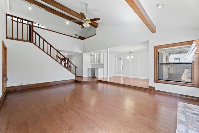 unfurnished living room featuring stairs, wood finished floors, beamed ceiling, and ceiling fan with notable chandelier