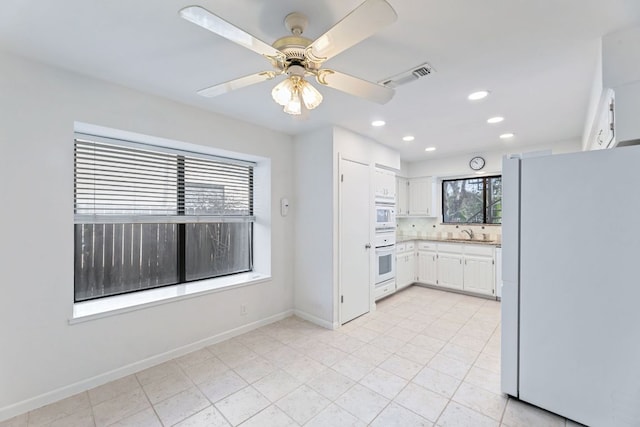 kitchen featuring white appliances, baseboards, visible vents, a sink, and white cabinets