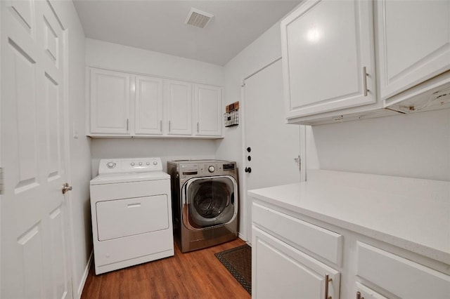 laundry room featuring washer and clothes dryer, visible vents, cabinet space, and wood finished floors