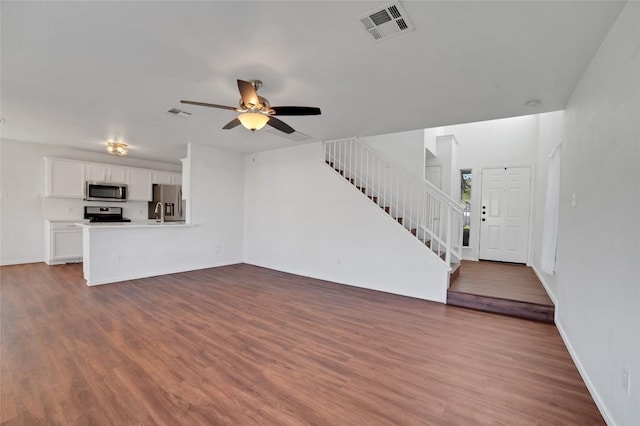 unfurnished living room featuring visible vents, baseboards, stairs, wood finished floors, and a ceiling fan