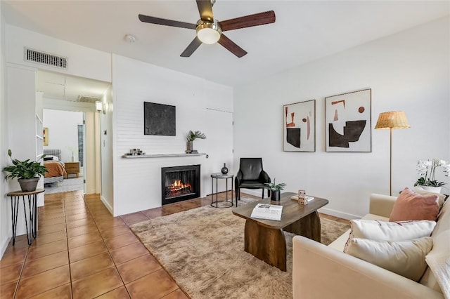 tiled living area with visible vents, a lit fireplace, and a ceiling fan