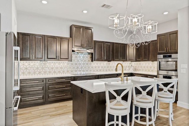 kitchen featuring visible vents, a sink, under cabinet range hood, appliances with stainless steel finishes, and tasteful backsplash