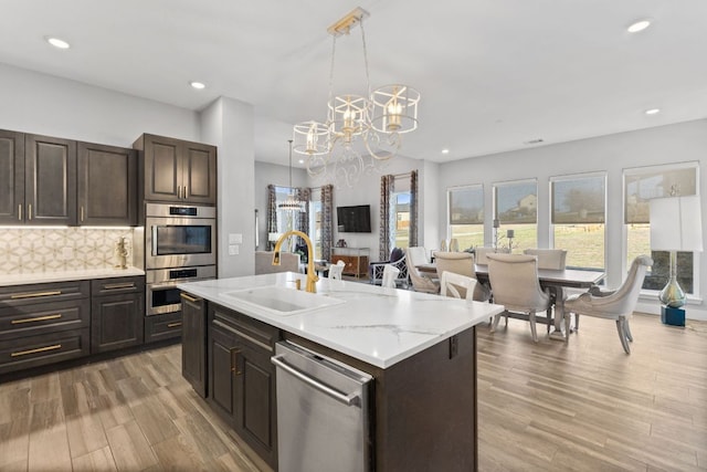 kitchen featuring light wood-type flooring, a notable chandelier, a sink, stainless steel appliances, and decorative backsplash