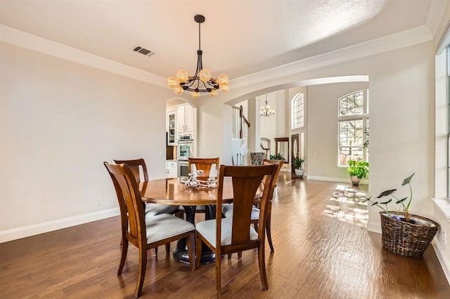 dining area with arched walkways, a notable chandelier, visible vents, and wood finished floors