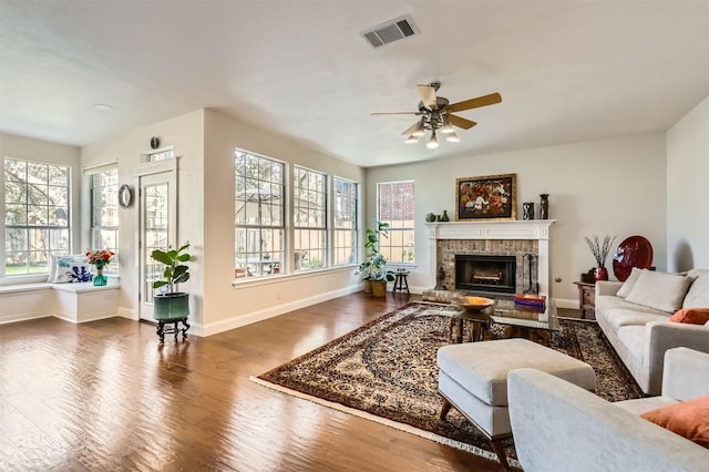 living room featuring visible vents, a fireplace with raised hearth, wood finished floors, and a ceiling fan