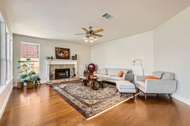 living room featuring a ceiling fan, wood finished floors, visible vents, baseboards, and a fireplace