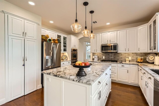 kitchen featuring stainless steel appliances, arched walkways, backsplash, and white cabinetry