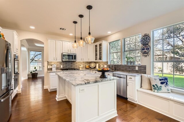 kitchen featuring backsplash, light stone counters, stainless steel appliances, arched walkways, and white cabinetry