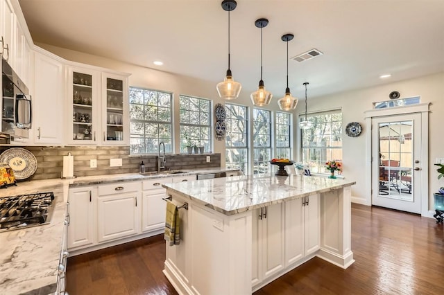 kitchen with visible vents, a kitchen island, a sink, appliances with stainless steel finishes, and tasteful backsplash