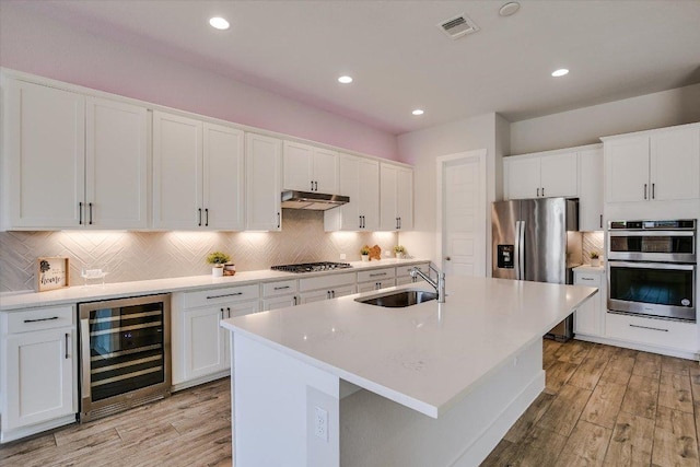 kitchen featuring visible vents, wine cooler, under cabinet range hood, stainless steel appliances, and a sink