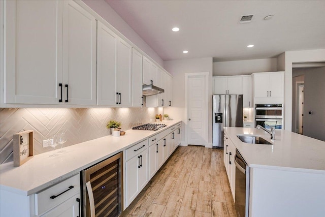 kitchen featuring visible vents, wine cooler, under cabinet range hood, appliances with stainless steel finishes, and a sink