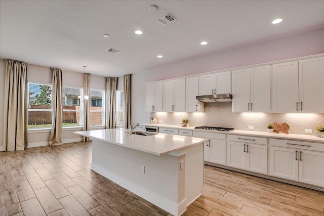 kitchen featuring visible vents, under cabinet range hood, stainless steel gas stovetop, white cabinets, and a sink