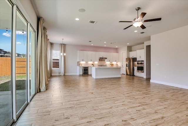 unfurnished living room with visible vents, light wood-style flooring, recessed lighting, wine cooler, and ceiling fan