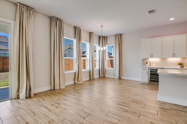 unfurnished dining area with light wood finished floors, visible vents, baseboards, wine cooler, and recessed lighting