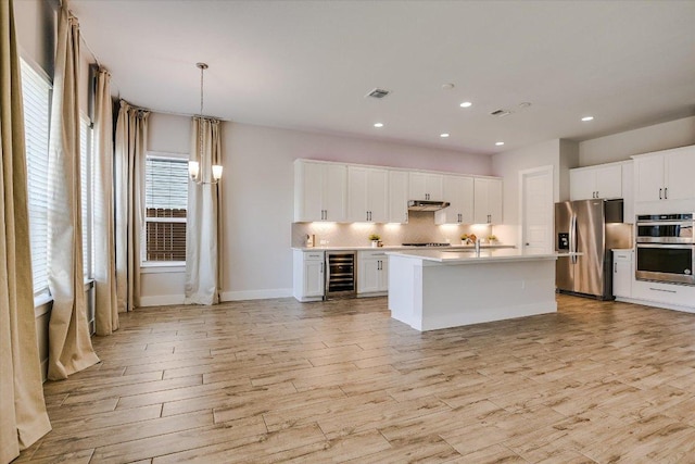 kitchen with beverage cooler, visible vents, light wood finished floors, decorative backsplash, and appliances with stainless steel finishes