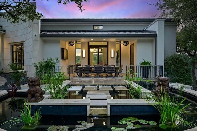 back of property at dusk featuring stucco siding, metal roof, and a standing seam roof