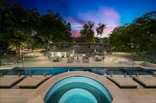 pool at dusk with a patio area, a fenced in pool, an in ground hot tub, and fence